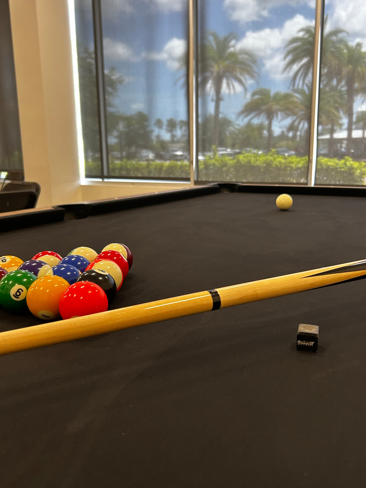 Pool table with racked balls and cue overlooking palm trees at the Teen Lounge inside The Link